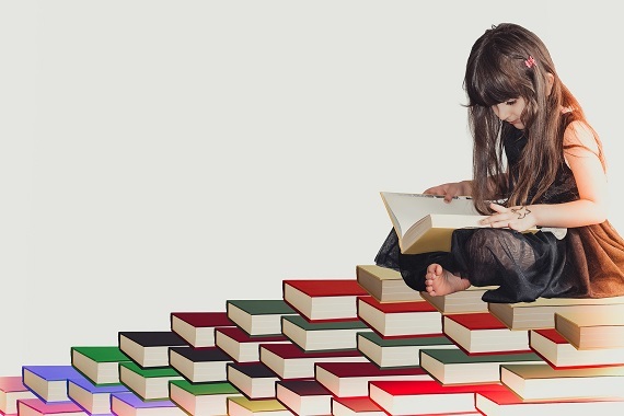 Meisje zit op boeken en houdt een boek vast dat ze leest.