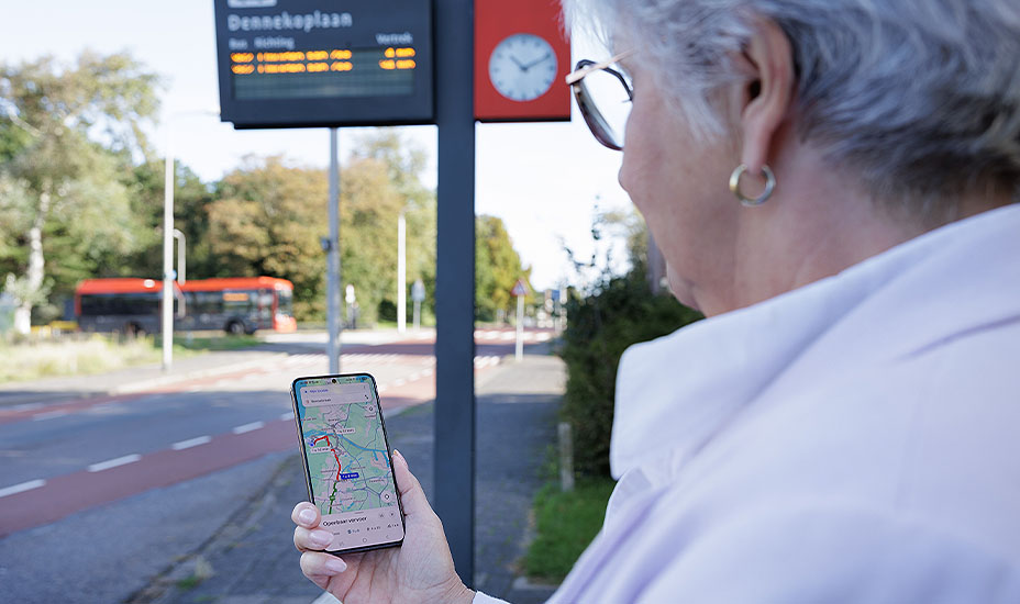 Reiziger kijkt op reisapp en op de achtergrond rijdt een bus