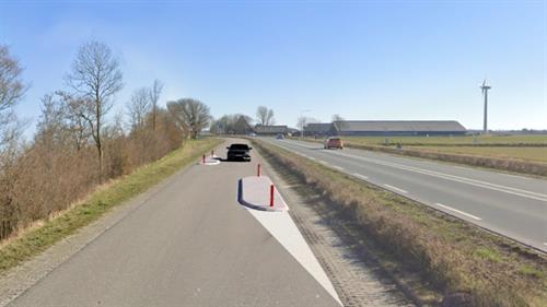 Parallelweg waar 2 slingers in de weg zijn geplaatst, een zwarte auto nadert.